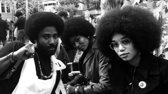 This may contain: two people with afro hair sitting next to each other in front of a group of people