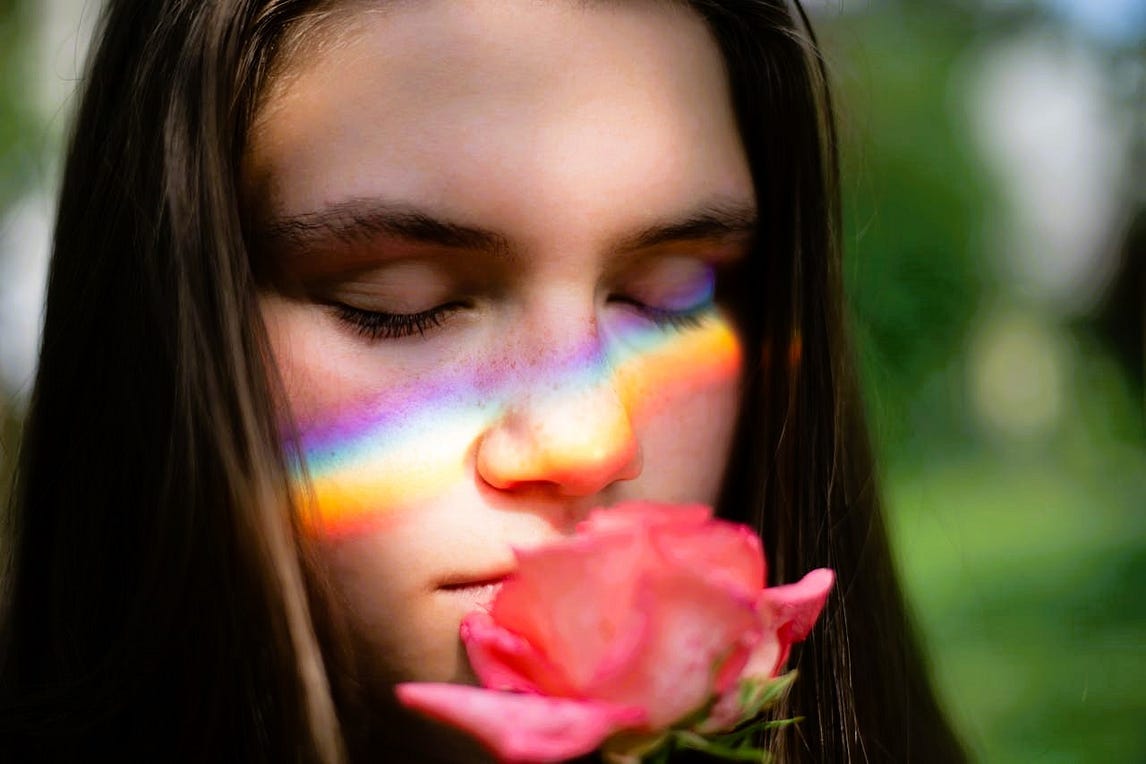 Woman smelling a rose with the reflection of a rainbow across her face