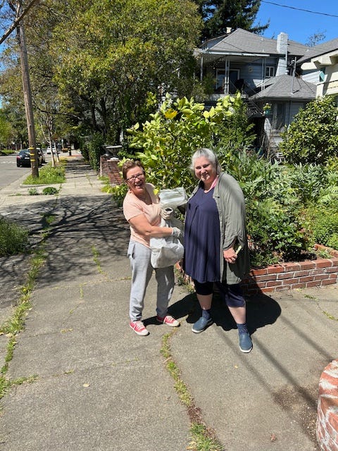 two smiling white women, casual dress, one is holding a 3-ft lemon shrub; both are smiling/laughing