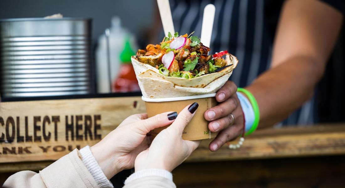 A hand passing down a taco bowl down to another pair of hands, with a wooden desk in front of them