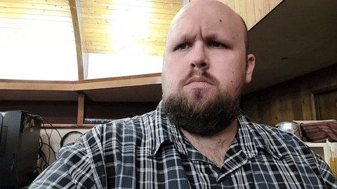 A bearded man looks startled and clutches at his throat as if clutching pearls.