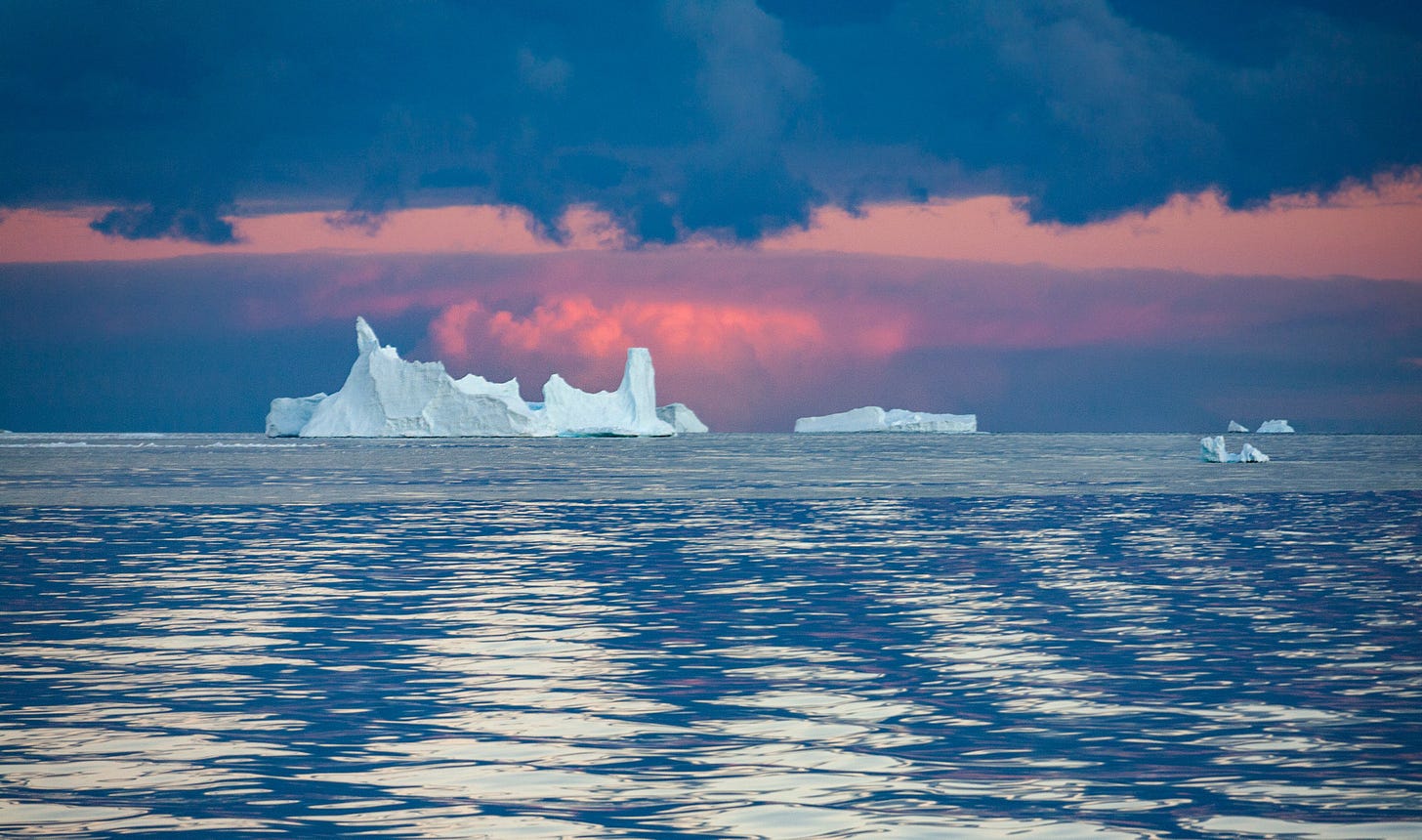 A massive white iceberg floats in the choppy blue waters of the Drake Passage under a soft pink and grey twilight sky.