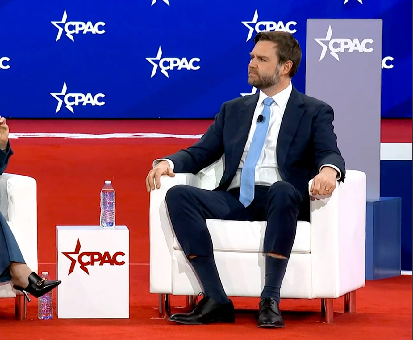 JD Vance sits in a chair at CPAC, wearing what appears to be the businessman equivalent of skinny jeans. His cuffs have hiked up above his socks, and there is no rational explanation for the slenderness of the cut.