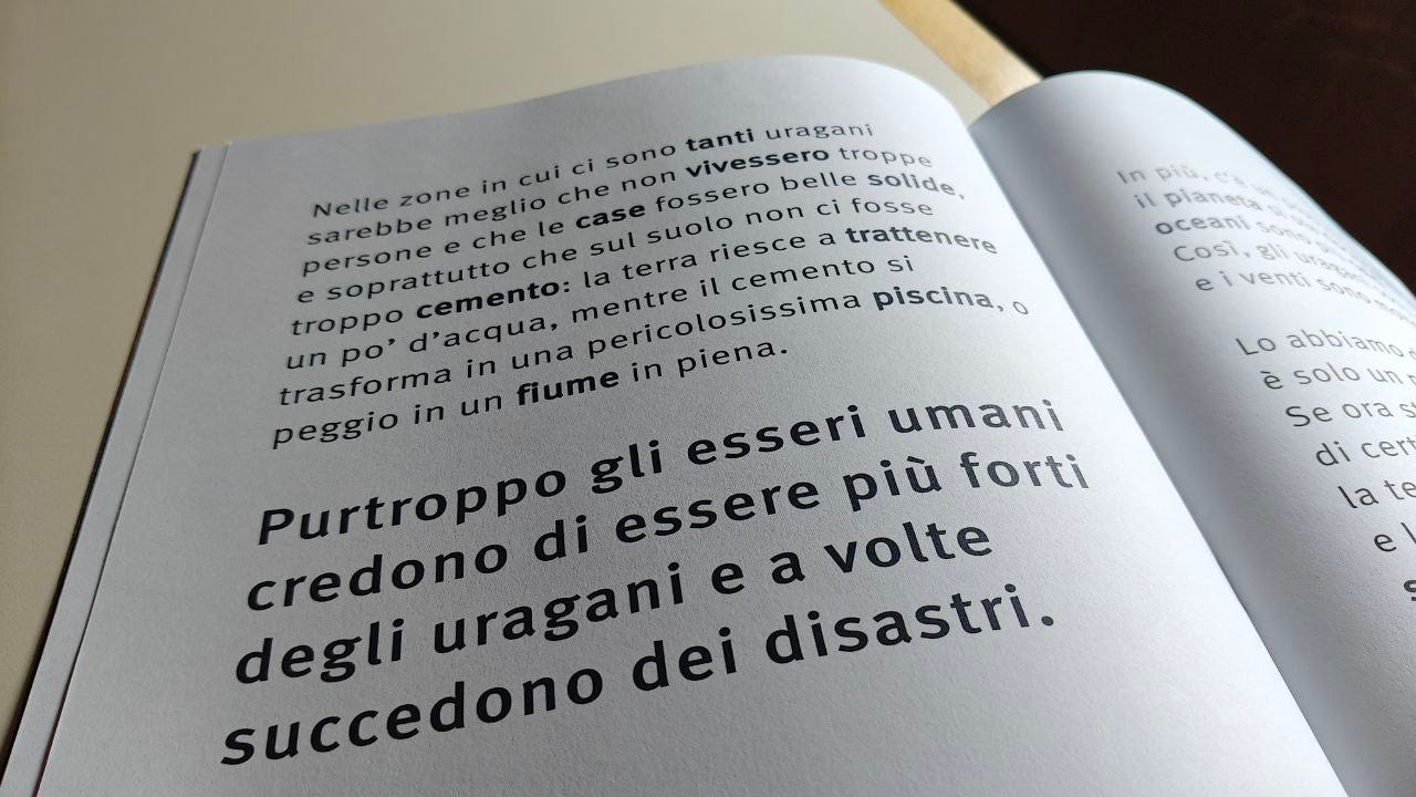 Pagina aperta della Scatolina URAGANO edita da effequ e scritta da Caterina Orsenigo. Pagina di un libro aperta che mostra un testo stampato in bianco e nero. Un paragrafo in alto, scritto con un carattere più piccolo, parla dei pericoli degli uragani e di come la cementificazione del suolo possa peggiorare i danni. Un altro paragrafo, con un carattere molto più grande e in grassetto, recita: 'Purtroppo gli esseri umani credono di essere più forti degli uragani e a volte succedono dei disastri'.