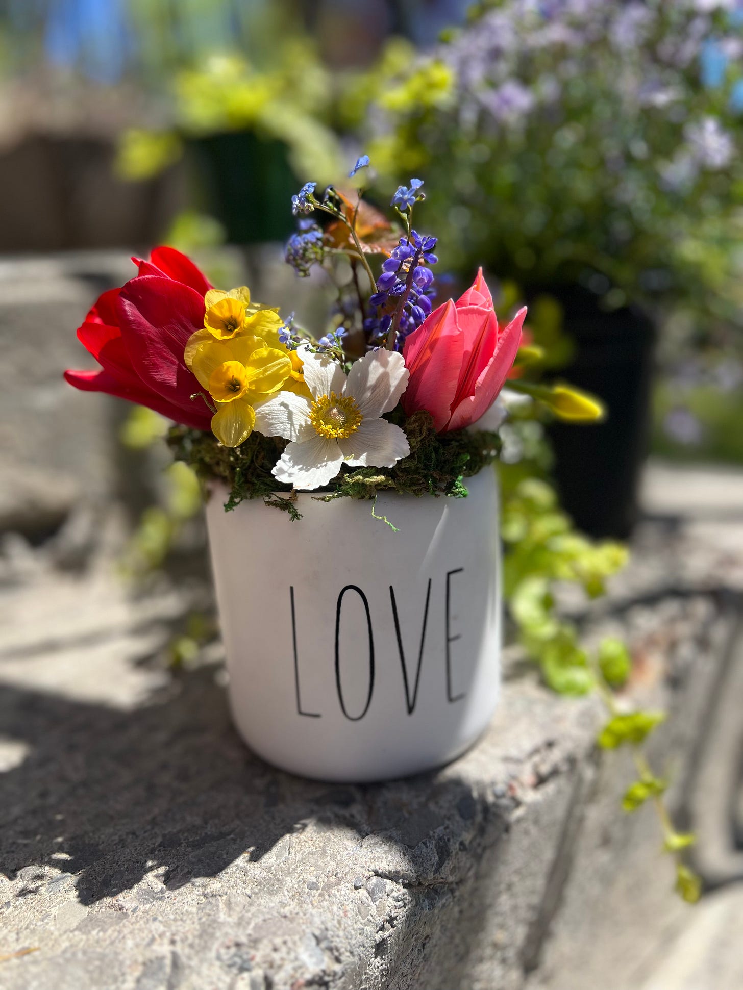 Vase of spring flowers in a white container with the words LOVE on the side.