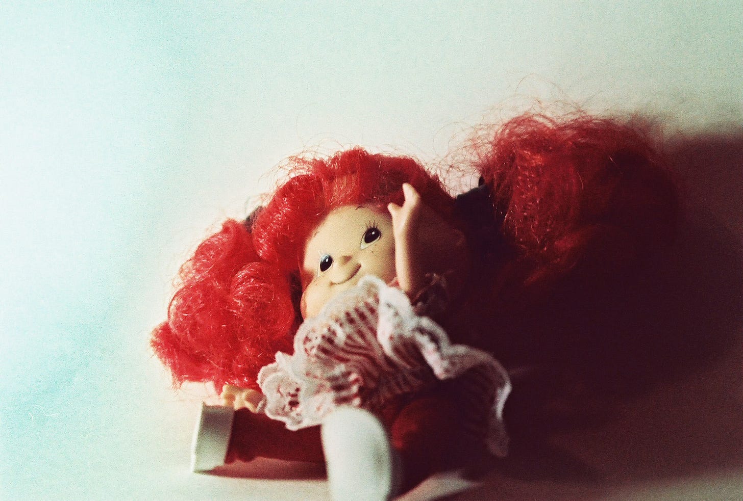 A film photo of a Strawberry Shortcake doll, lying on her back haphazardly with her left arm sticking up in the air. 