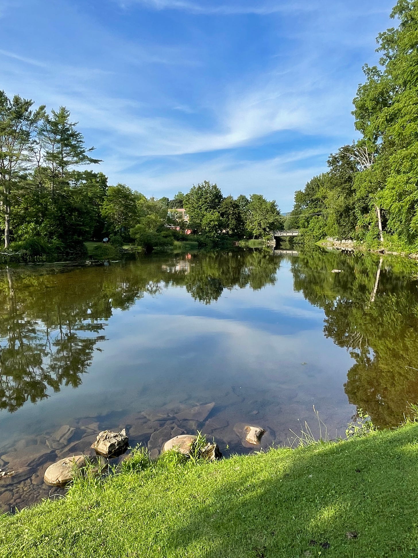 Bennington, Vermont a pond showing a reflection of the surrounding green trees and a clear blue sky. 