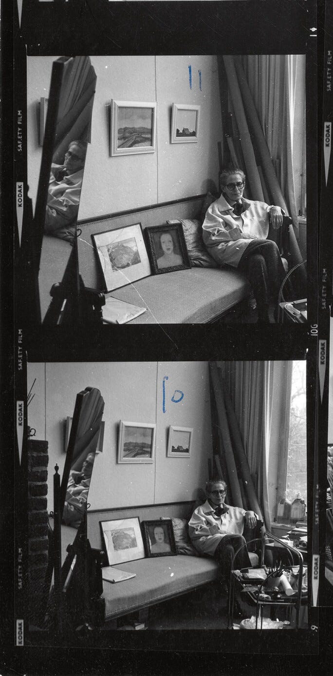 A black and white image shows Gluck sitting on a sofa in a cozy room with framed art and photographs on the wall and sofa. The atmosphere is relaxed. There are 2 images together, the top one labelled 11, and the other labelled 10. There is a mirror on the left side that is reflecting Gluck in it. They are sitting on the couch in their smock, and some pants, with their left arm resting on the couch arm. There is a small table in front of them with some plants and other decor on it. To their left, there is a large window with some curtains pulled to the side. Gluck is wearing glasses and they have a slight smile on their face. A black and white image shows Gluck sitting on a sofa in a cozy room with framed art and photographs on the wall and sofa. The atmosphere is relaxed. There are 2 images together, the top one labelled 11, and the other labelled 10. There is a mirror on the left side that is reflecting Gluck in it. They are sitting on the couch in their smock, and some pants, with their left arm resting on the couch arm. There is a small table in front of them with some plants and other decor on it. To their left, there is a large window with some curtains pulled to the side. Gluck is wearing glasses and they have a slight smile on their face.