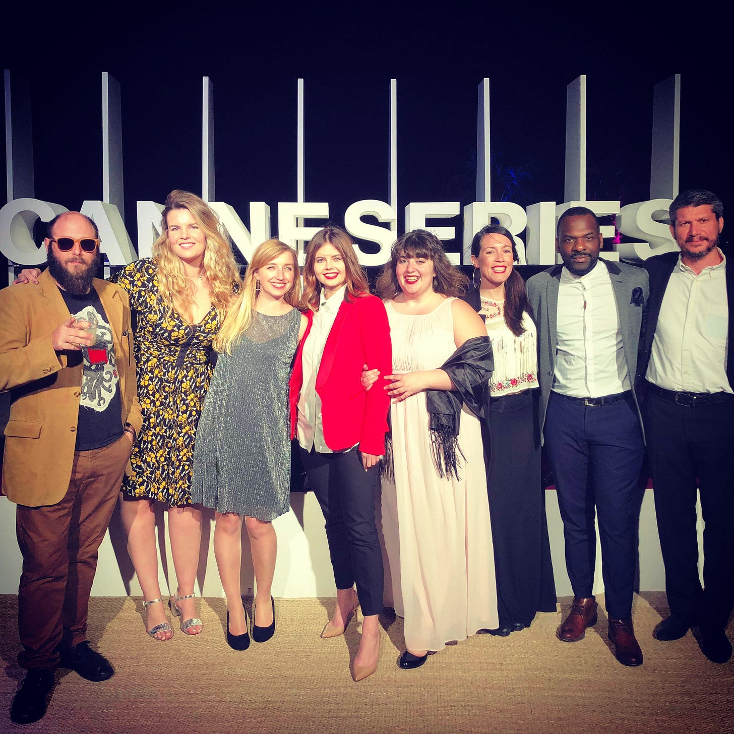 Group photo at the CannesSeries event featuring eight people standing in front of a large “CANNESERIES” sign. Sophie McVeigh is third from the left, wearing a sparkly dress and smiling with fellow writers and creatives. Group photo at the CannesSeries event featuring eight people standing in front of a large “CANNESERIES” sign. Sophie McVeigh is third from the left, wearing a sparkly dress and smiling with fellow writers and creatives.
