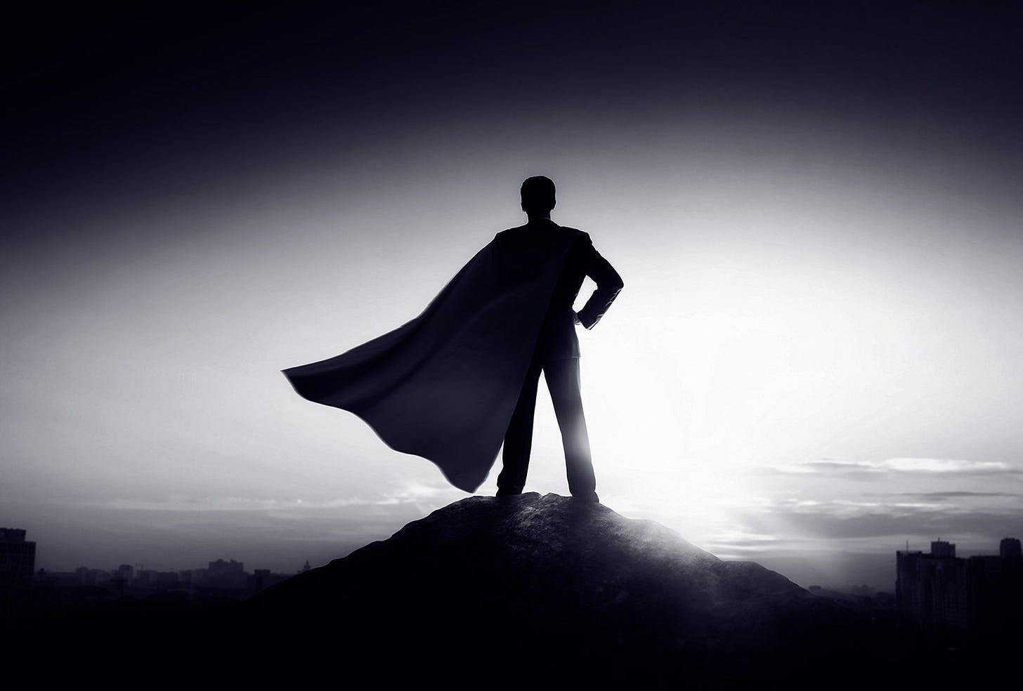 Image of unidentified superhero with back facing us wearing a cape. He is perched on a hill surveying the landscape