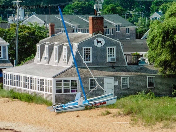 Photo of a two-story shingled building situated near a beach. The photo appears to have been taken from the deck of a Martha's Vineyard ferry. 