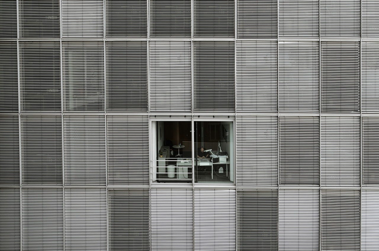 Side view of an office building. Only one room's window is open. The others all have their blinds down.
