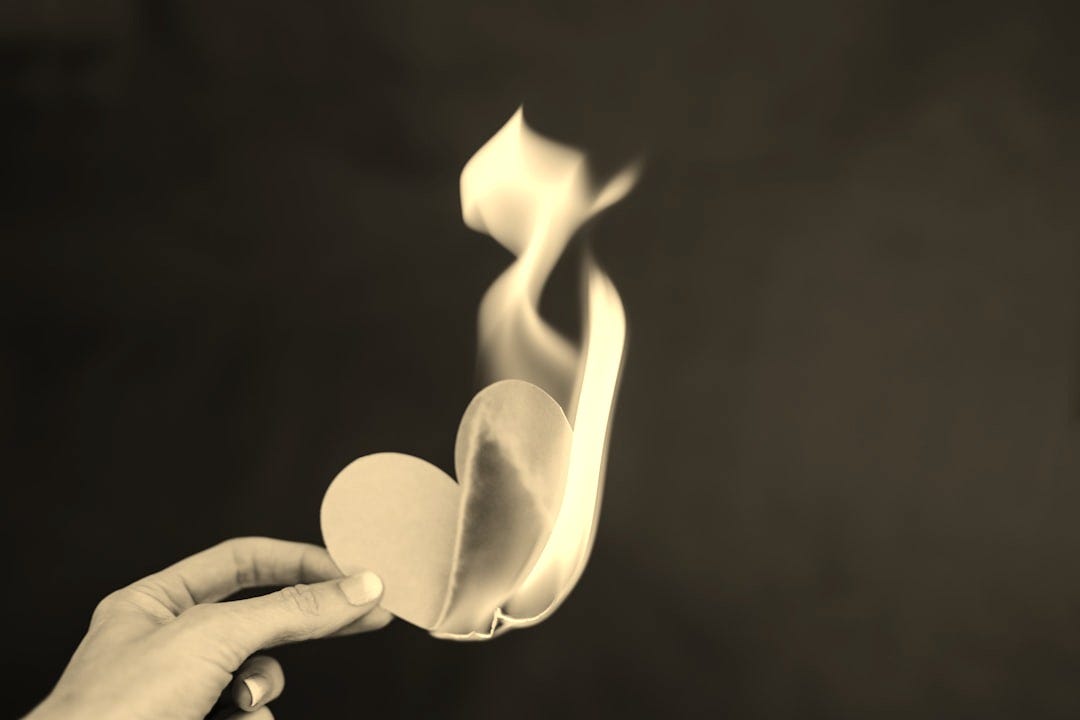 a person holding a paper heart in front of a fire