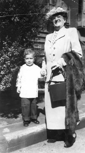 Black and white photo of a tall women with light skin and a hat on with a long fancy coat on and a mink over her arm. She is holding hands with a young boy, maybe 3 years old. Black and white photo of a tall women with light skin and a hat on with a long fancy coat on and a mink over her arm. She is holding hands with a young boy, maybe 3 years old.