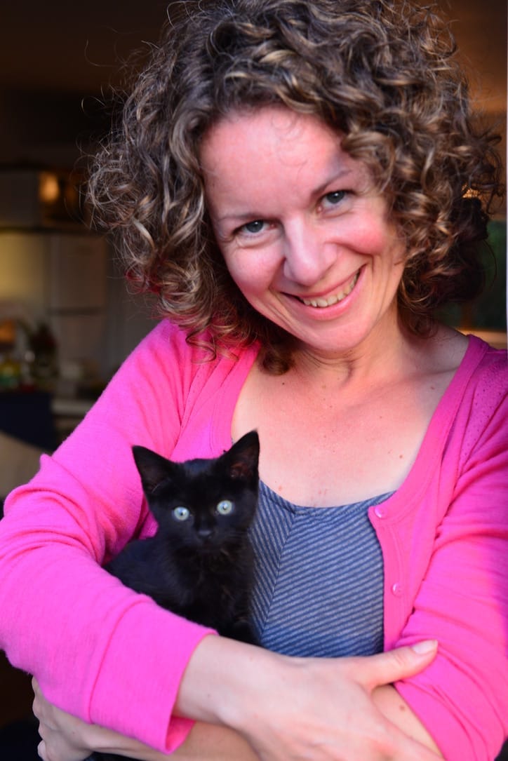 Janelle Hardacre is smiling and holding a baby black kitten in her arms. Janelle Hardacre is smiling and holding a baby black kitten in her arms.