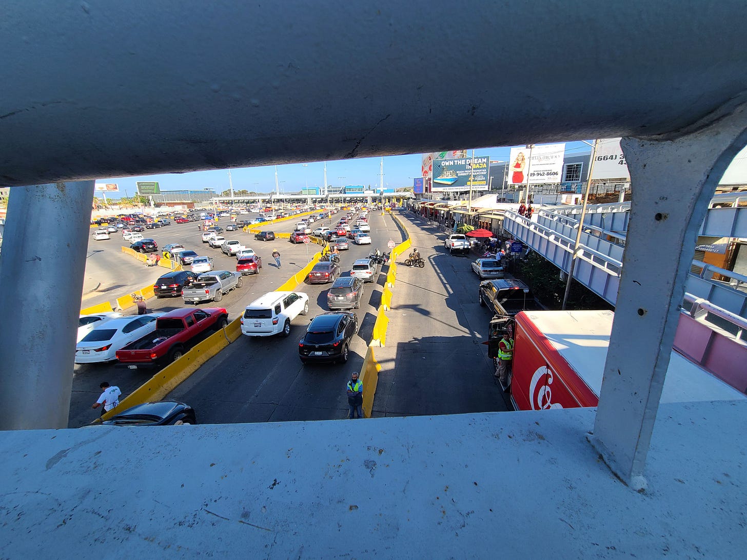 A guardrail frames a view of cars in line between low yellow walls in front of booths