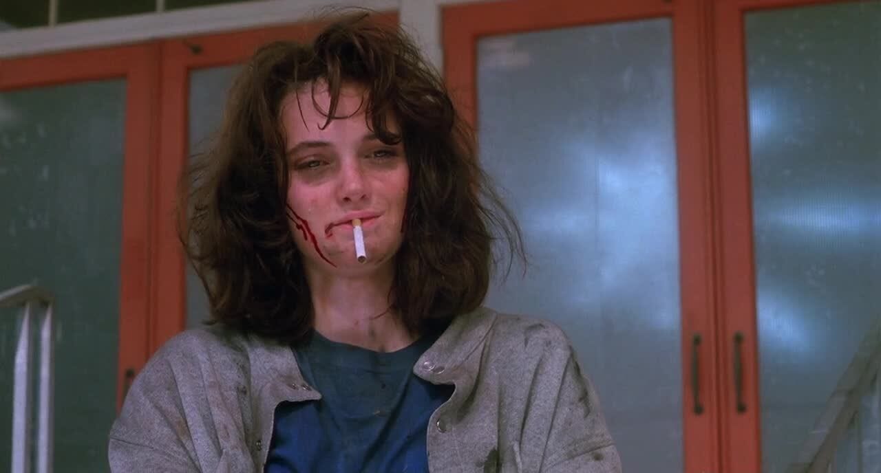 A very grizzled, bloody Winona Ryder with a cigarette in her mouth from the movie HEATHERS