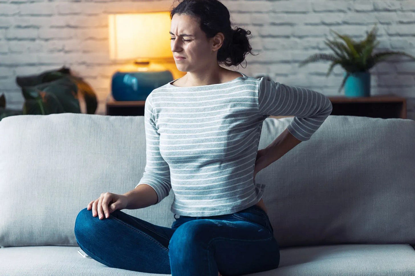 Young woman at home grimmasing in back pain, holding her arm on lower back