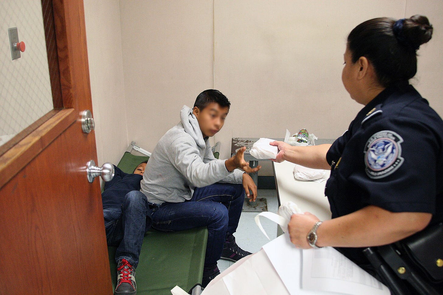 A CBP officer speaks with an unaccompanied minor seated in a processing room A CBP officer speaks with an unaccompanied minor seated in a processing room