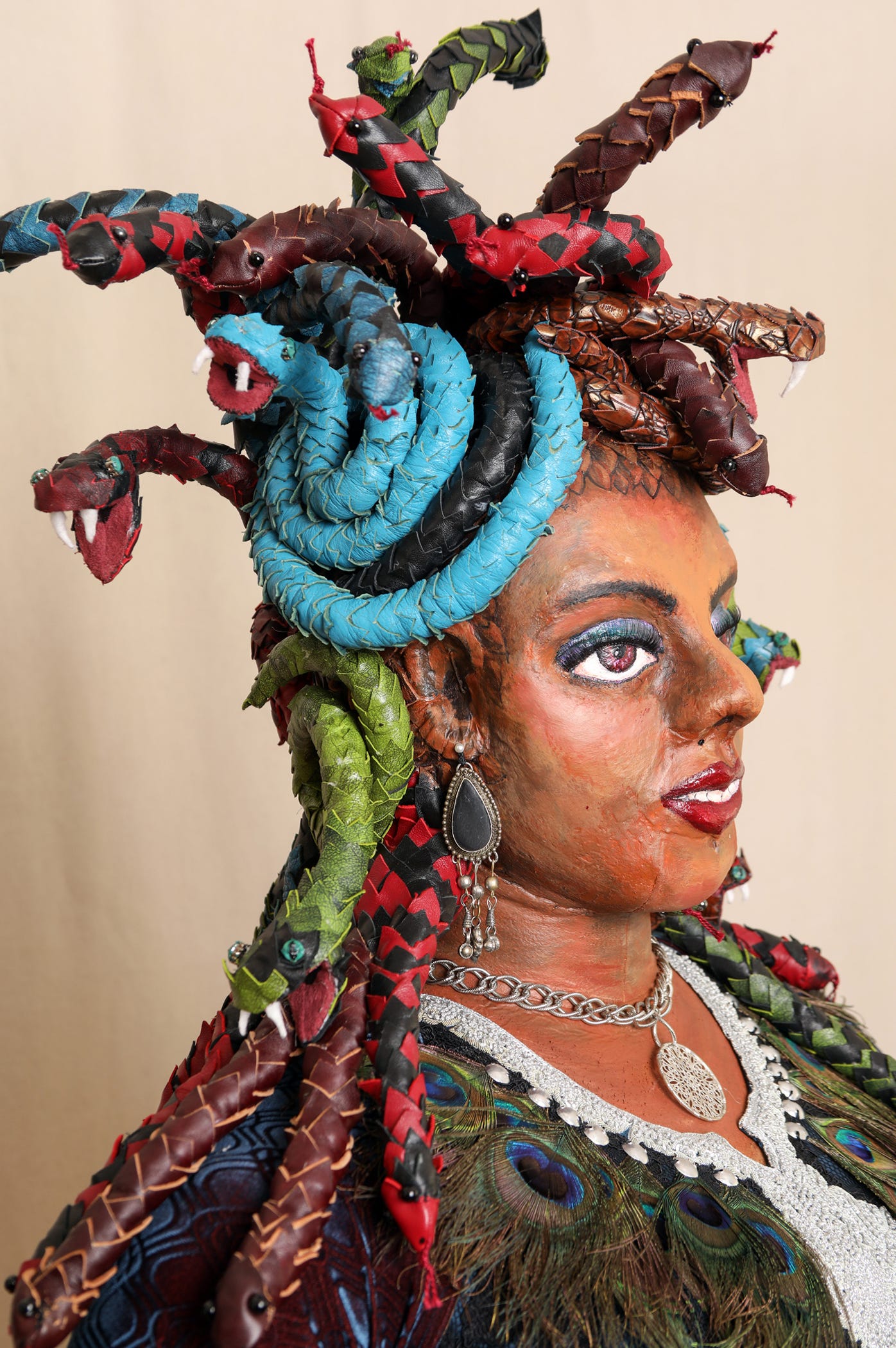 Sculpted head and bust of a browns skinned woman with multicolored snakes for hair and a peacock feather necklace.