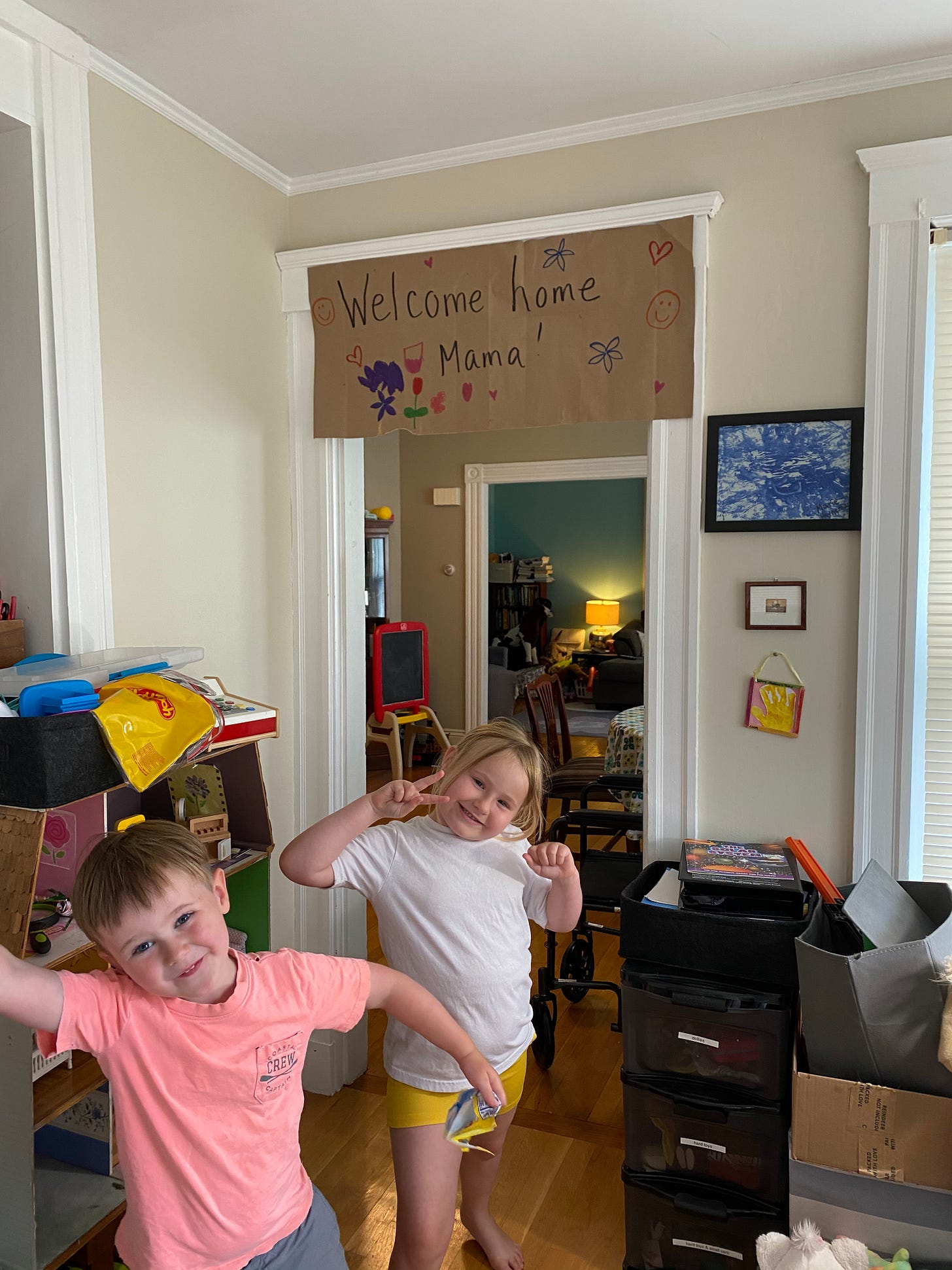2 young white children smile in front of a sign that reads welcome home mama