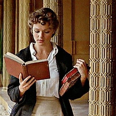 This may contain: a woman is reading a book while standing in an archway with columns and pillars behind her