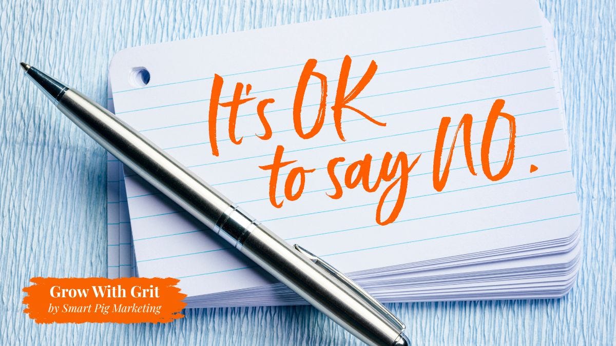 A lined index card beside a silver pen displays the handwritten message "It's OK to say no." The image represents setting healthy boundaries, protecting time and energy, and making intentional business decisions without feeling guilty. The Grow With Grit by Smart Pig Marketing logo appears in the lower-left corner.