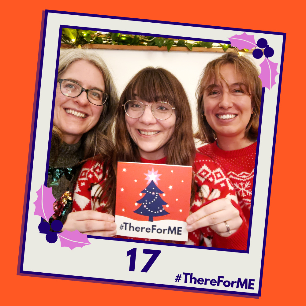 A pretend polaroid shows Emma, Karen and Oonagh in their Christmas jumpers, smiling and posing for a photo holding a #ThereForME Christmas card.   The image on the card shows the dark blue Christmas tree, decorated with sparkling fairy lights, baubles and a star on the top, in a snowy landscape against a starry backdrop. The design is in the #ThereForME colours.