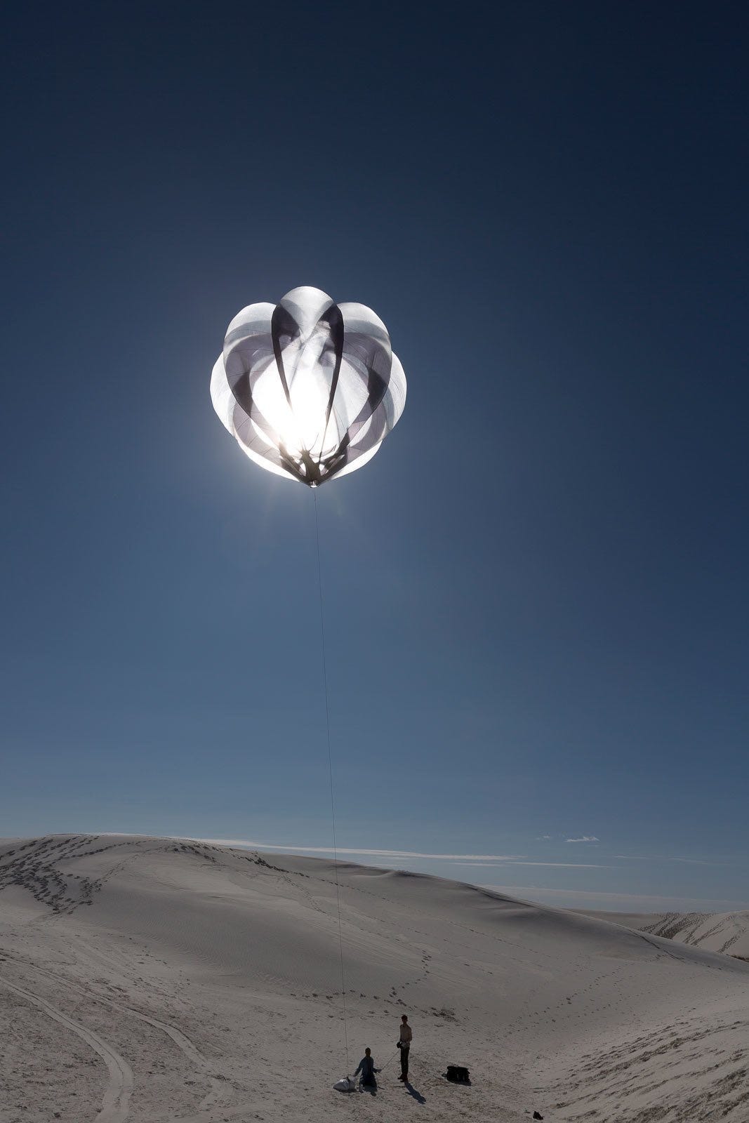 A hot air balloon being released into a bright blue sky by two people working with Aerocene.
