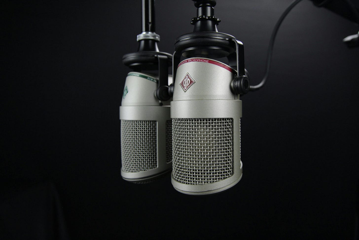 Two silver microphones on a black swing arm stand, in a dark room.