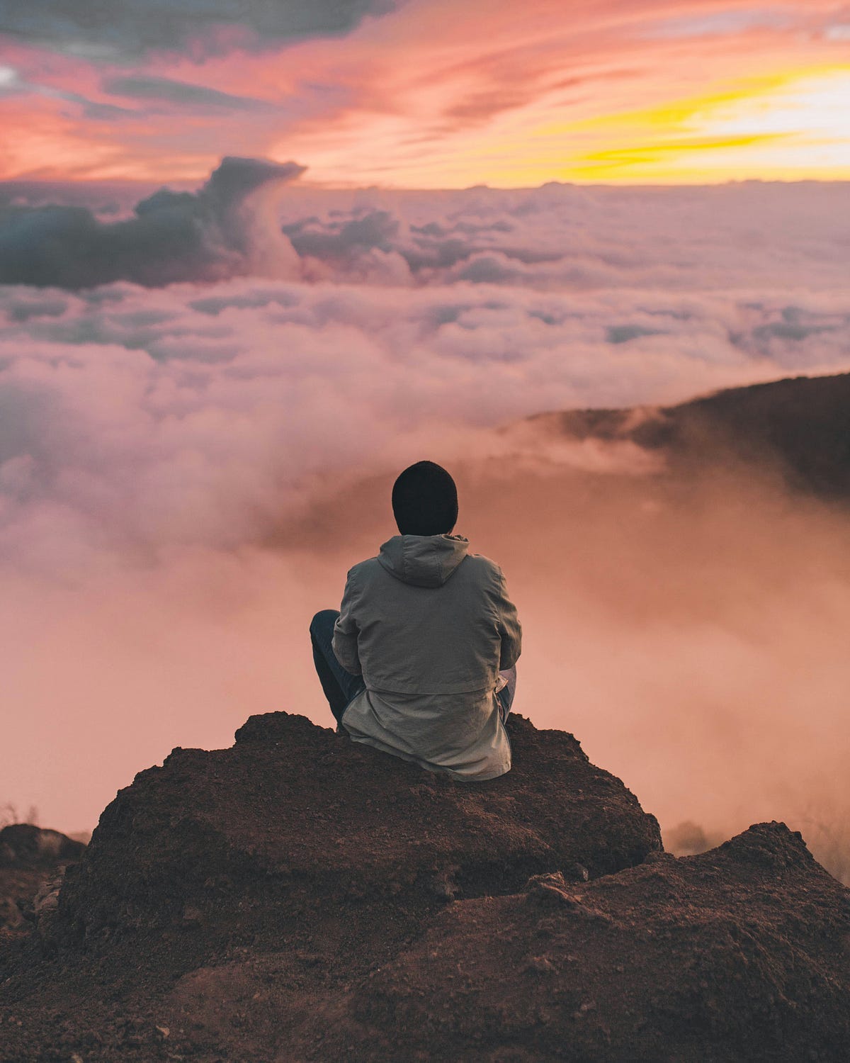 Person sitting on a mountain looking at the clouds