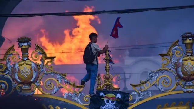 A man is hanging a pirate flag as smoke and flames rise from the Singha Durbar.