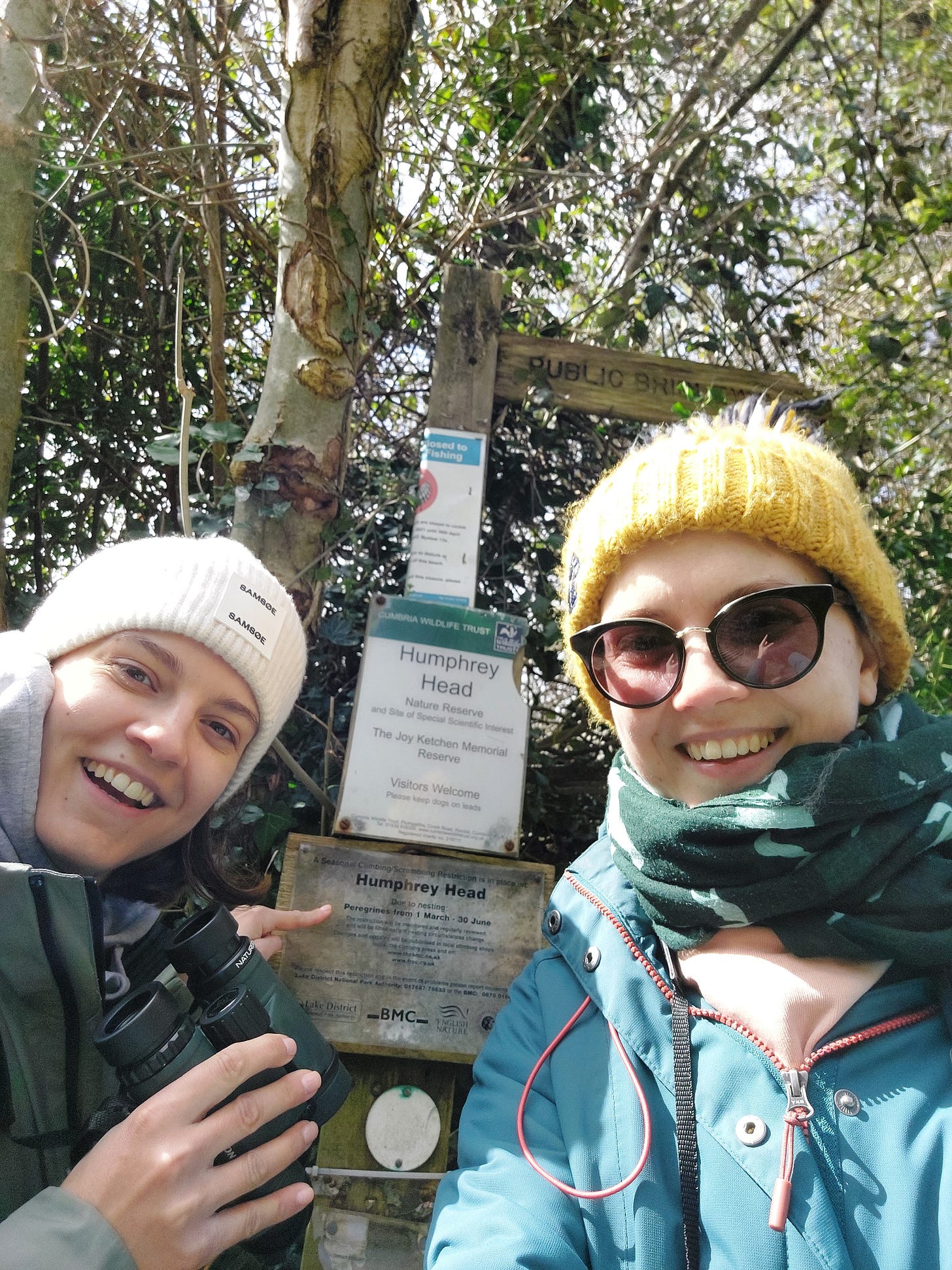 Two very smiley sisters pointing at the Humphrey Head falcon sign