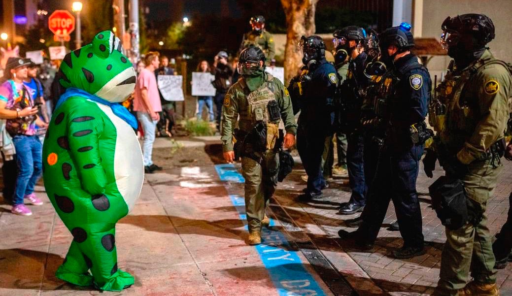 A protester in a frog costume stands in front of a line of federal law enforcement officers outside an ICE facility in Portland, Oregon.