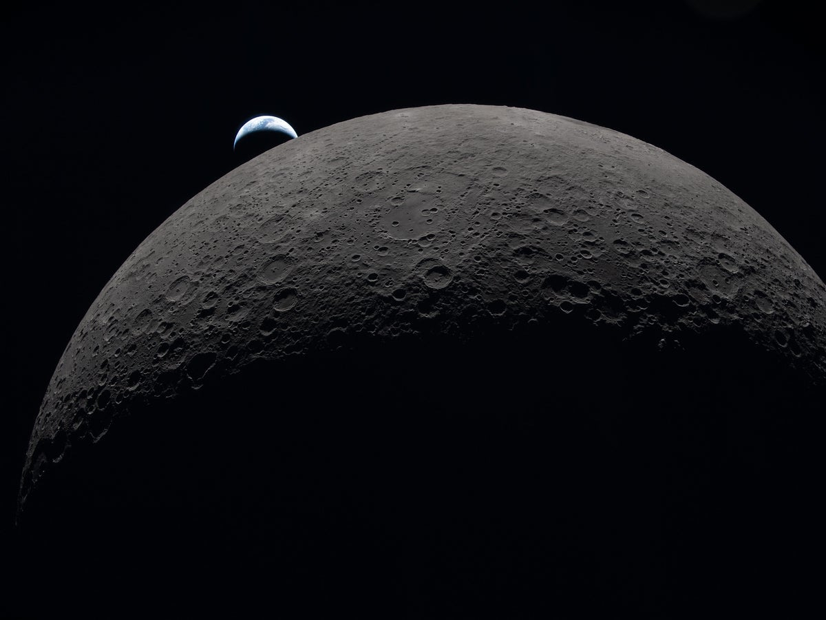 Photo of earth peeking out from behind a giant moon, taken by the Artemis II crew