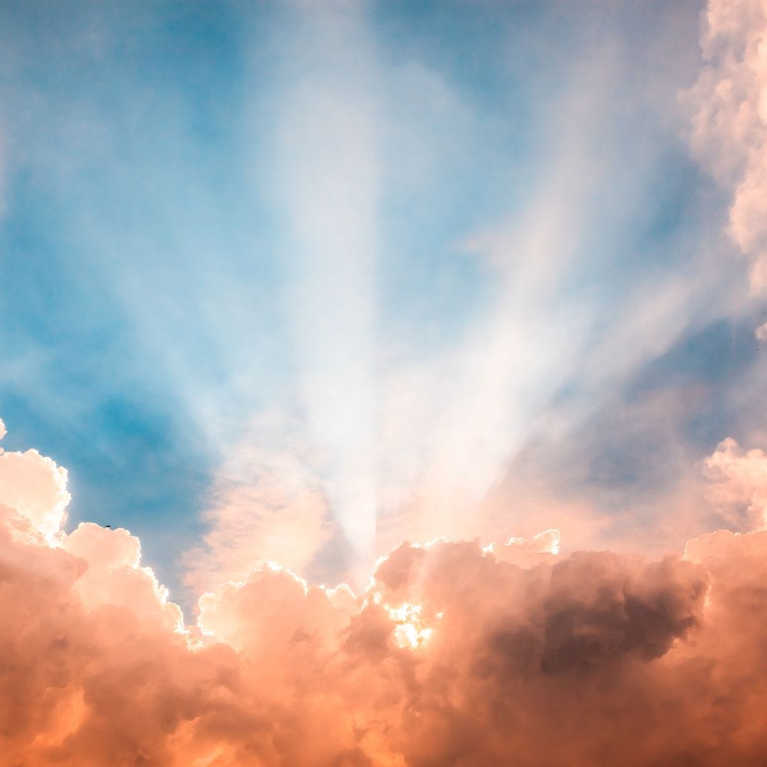 pink and white clouds with sun behind them casting rays of light into a blue sky via Canva