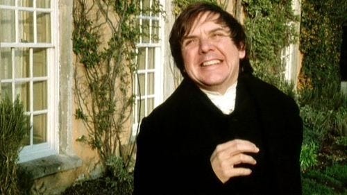 This may contain: a man standing in front of a house with his arms crossed and eyes wide open