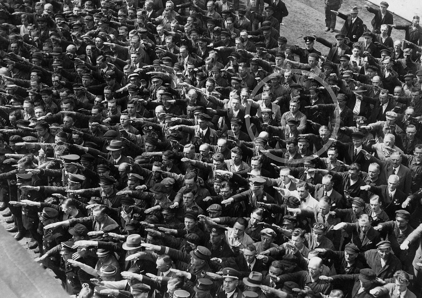 Photo of a crowd of people giving a nazi salute. One man stands there with his arms crossed, not participating.