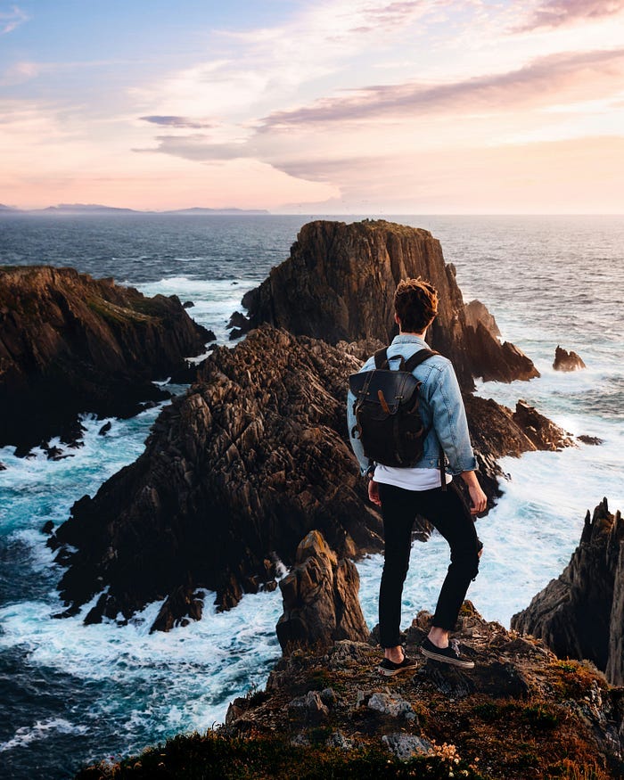 A man with a backpack stands looking out over a breathtaking view of ocean cliffs. A man with a backpack stands looking out over a breathtaking view of ocean cliffs.
