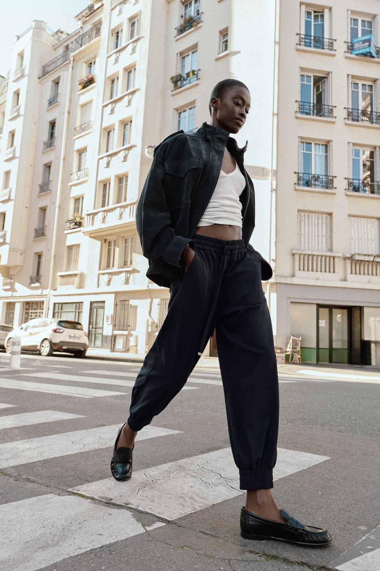 Black jacket, white T-shirt, and navy trousers with side pockets and elasticated cuffs. Black shoes.