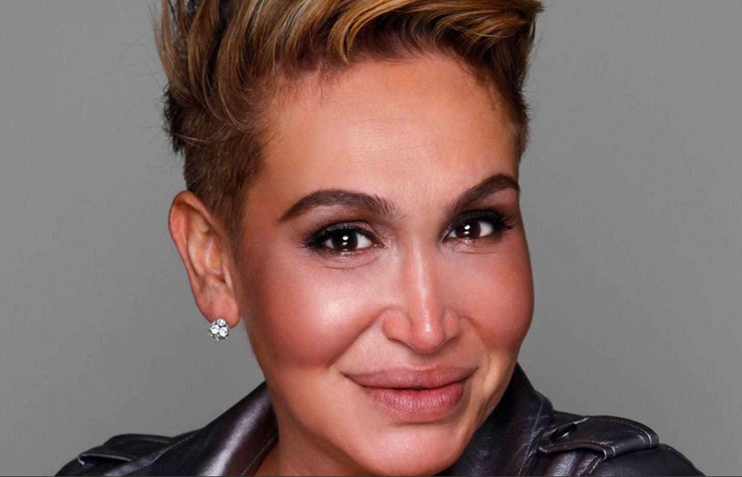 A close up head shot of my beautiful friend, Cecilia Gentili, a Latine femme of Argentinian descent smiling at the camera with knowledge and love in her eyes, hair short on the sides and risung up past the top of the frame. Her one visible ear has a sparling diamond stud earing, she is wearing makeup and you can see the very top of her black leather jacket with epaulettes. A close up head shot of my beautiful friend, Cecilia Gentili, a Latine femme of Argentinian descent smiling at the camera with knowledge and love in her eyes, hair short on the sides and risung up past the top of the frame. Her one visible ear has a sparling diamond stud earing, she is wearing makeup and you can see the very top of her black leather jacket with epaulettes.
