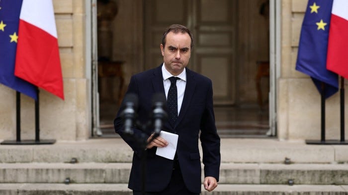 Sebastien Lecornu walks outside Hotel Matignon holding papers, with French and EU flags in the background.