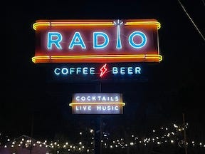 The neon sign for Radio Coffee and Beer, and the outdoor stage with mic stands and PA equipment, lit with blue light.
