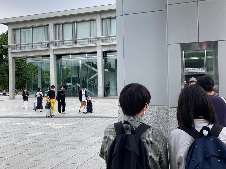 Long horizontal museum building with square arched windows. Arch in concrete plaza.