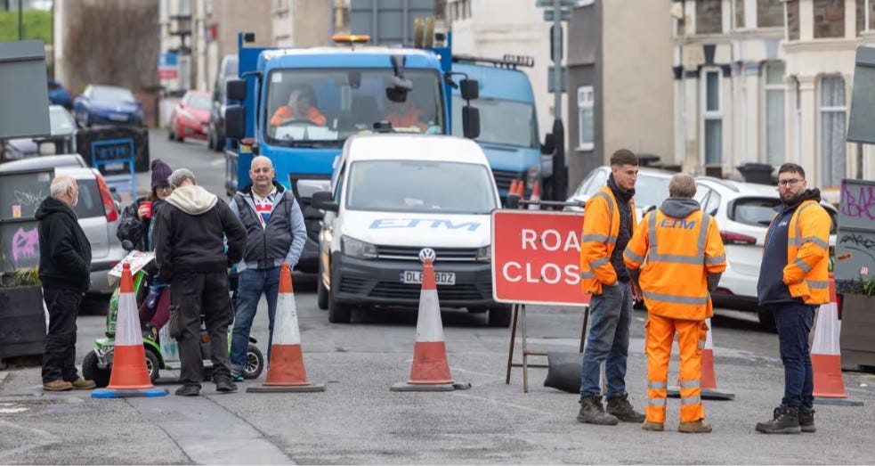 Residents block Avonvale Road in Barton Hill, Bristol, on 18 April 2026, preventing ETM contractors from installing a new bus gate as part of the East Bristol Liveable Neighbourhood trial. A Road Closed sign stands between residents and contractors during the standoff.