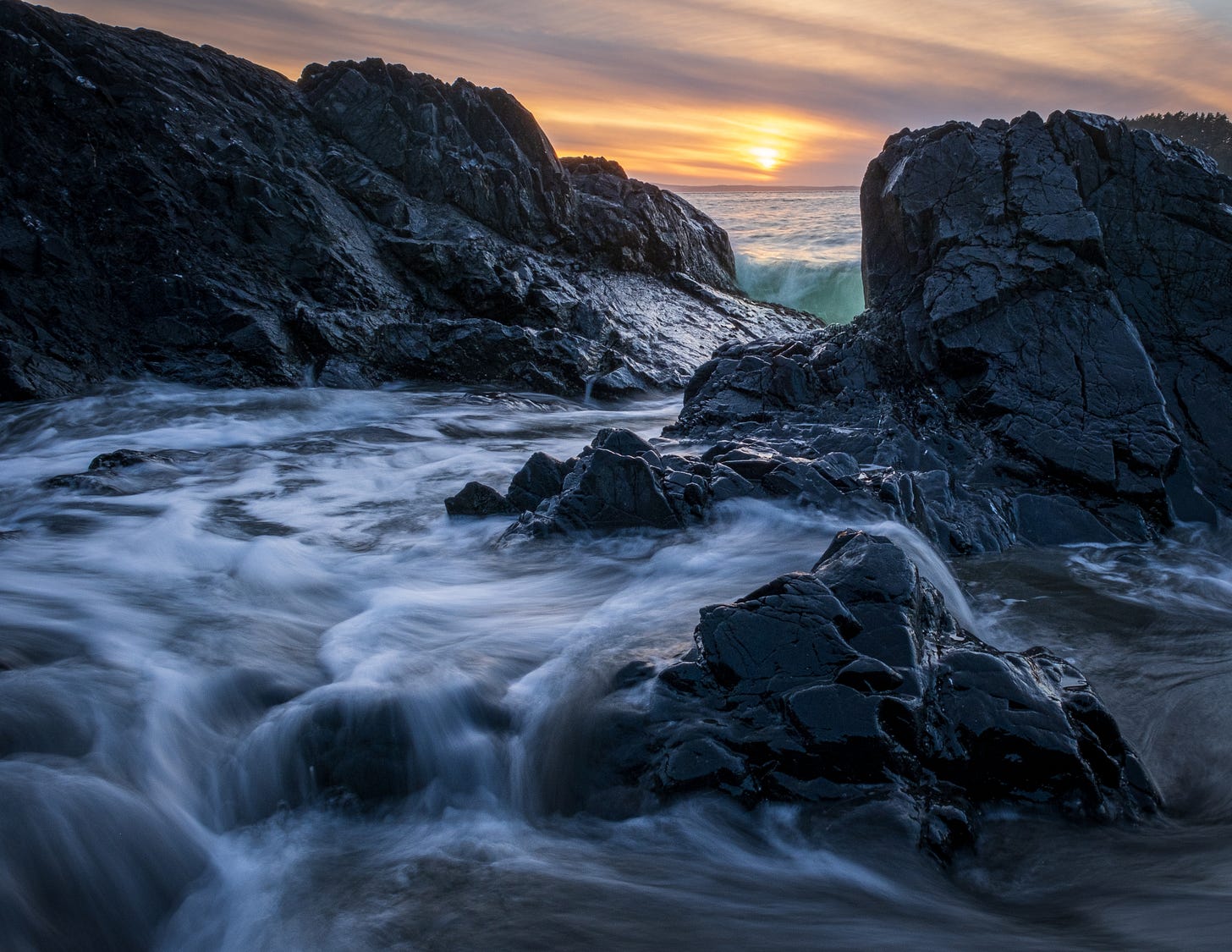 Rocks at sunset creating a small tide pool, photographed low to the ground and at a long exposure.