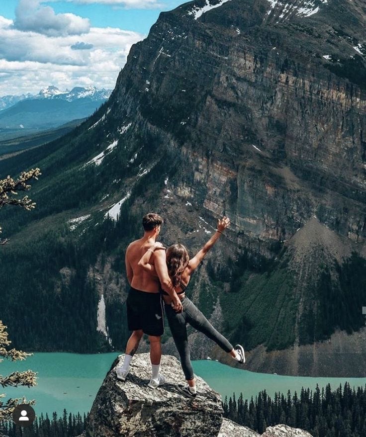 This may contain: two people standing on top of a mountain with their arms in the air and one person holding his leg up