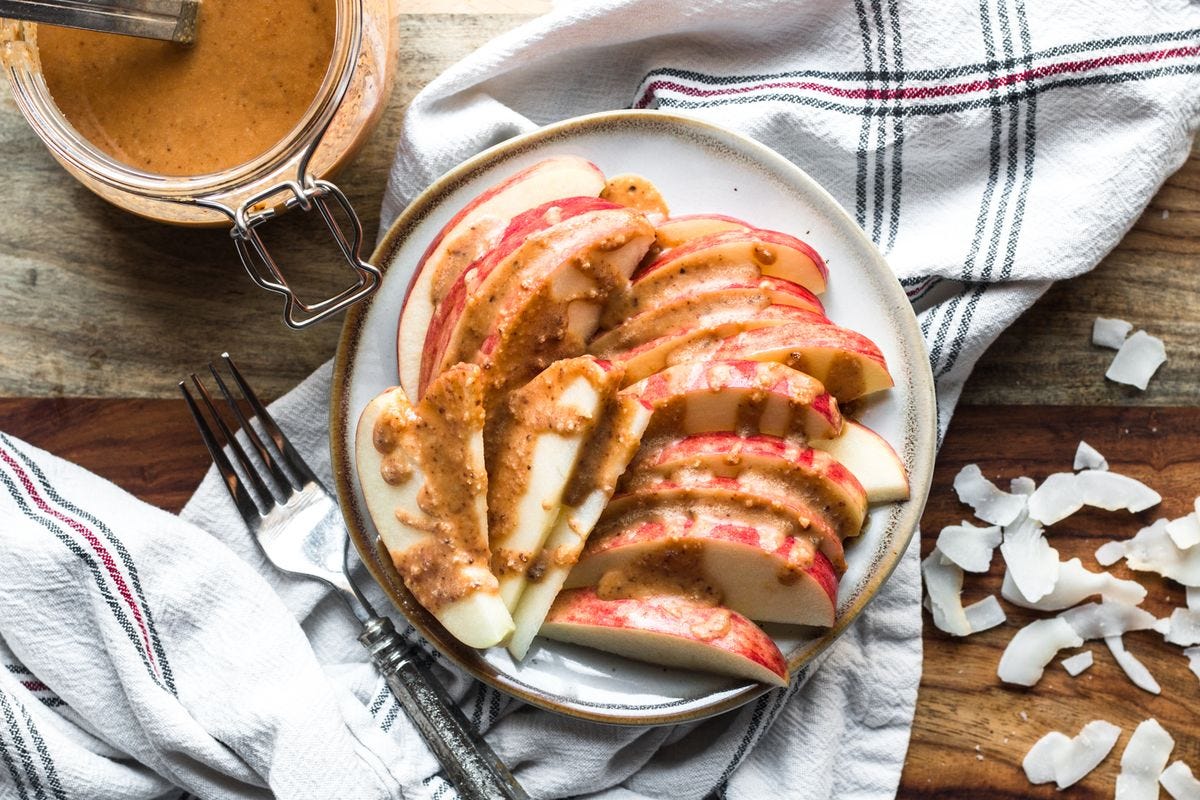 Apples on a plate drizzled with coconut butter alongside white kitchen towel, fork, jar of coconut butter, raw coconut flakes. Apples on a plate drizzled with coconut butter alongside white kitchen towel, fork, jar of coconut butter, raw coconut flakes.