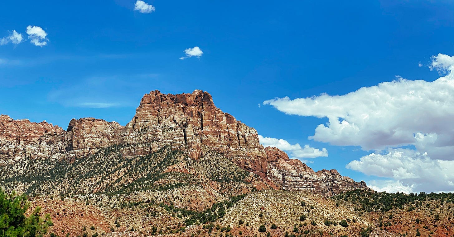 A rugged, red rock mountain with unique formations set against a bright blue sky with a few scattered clouds, capturing the essence of a desert landscape.