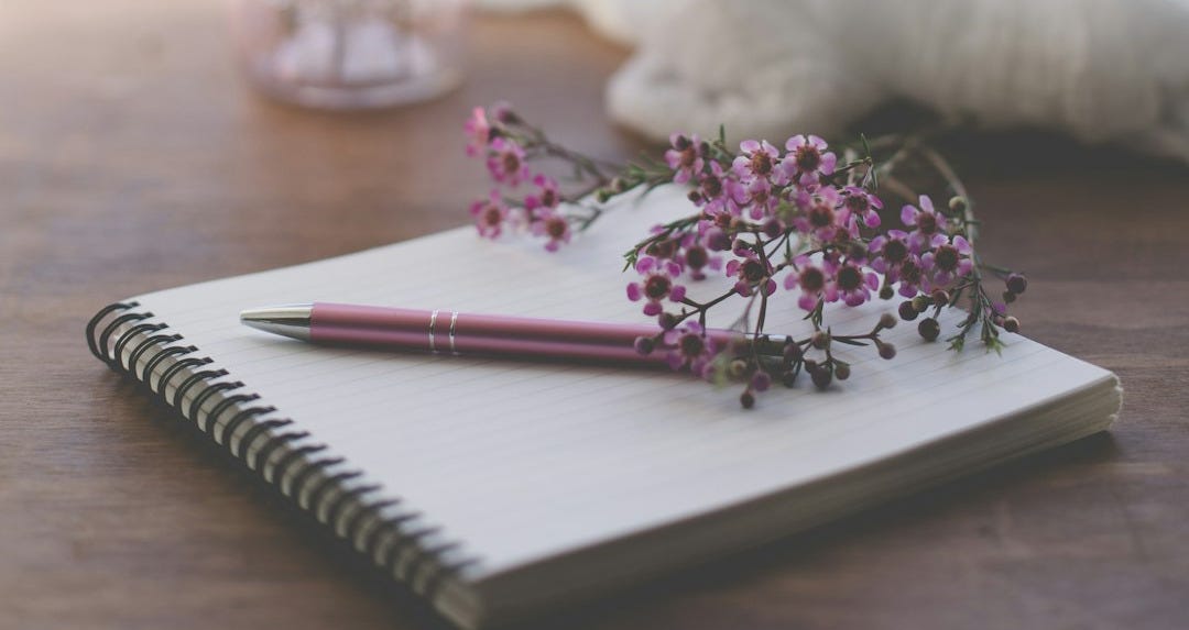 shallow focus photo of purple flowers on white spiral notebook shallow focus photo of purple flowers on white spiral notebook